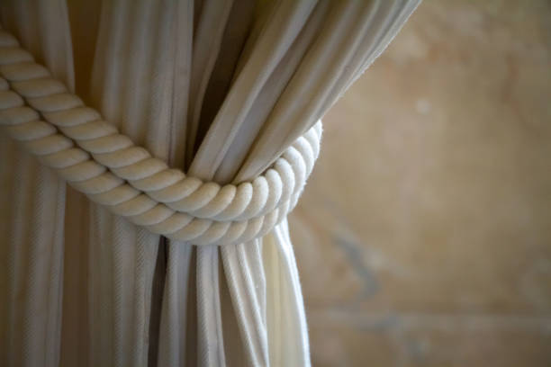 Close up drapery beige curtain tied with a large weave rope, selective focus