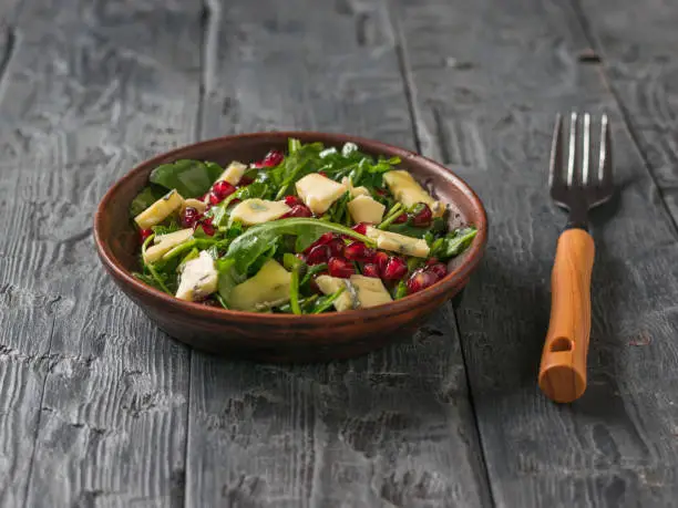 Fork and bowl with arugula, pomegranate and blue-mold cheese salad. Diet vegetarian salad.