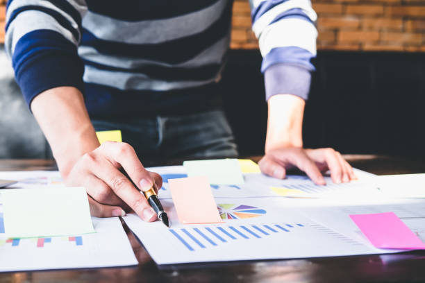 istock Asian business man hand holding note paper meeting with new startup project use post it notes to share idea discussion and analysis data charts and graphs.Business finances and accounting concept 1189045982