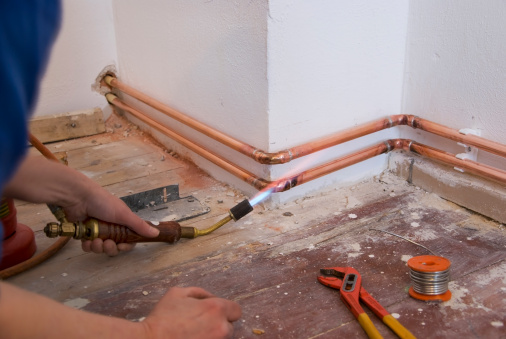 plumber soldering a copper pipe as part of aheating system