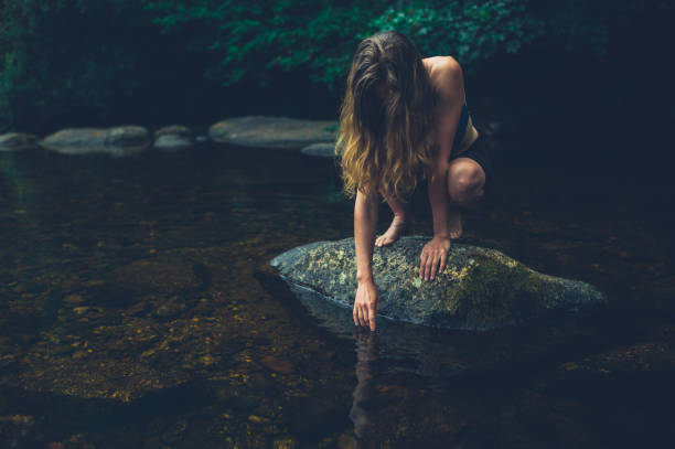 istock Young woman sitting on rock in a river 1189056717