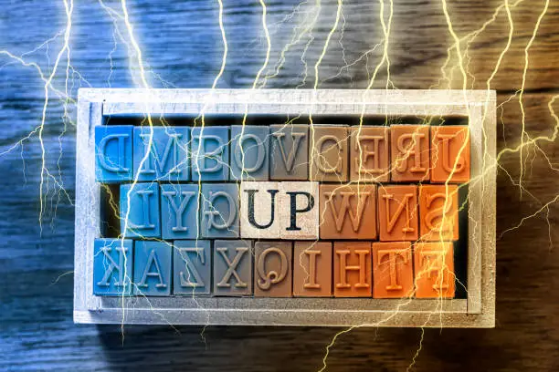 Photo of UP - isolated abstract in blue and orange wood type stamps and lightning or thunder against wooden background and copy space.