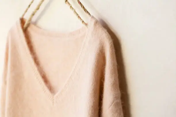 light pink sweater hanging on clothes hanger on white background.close up.