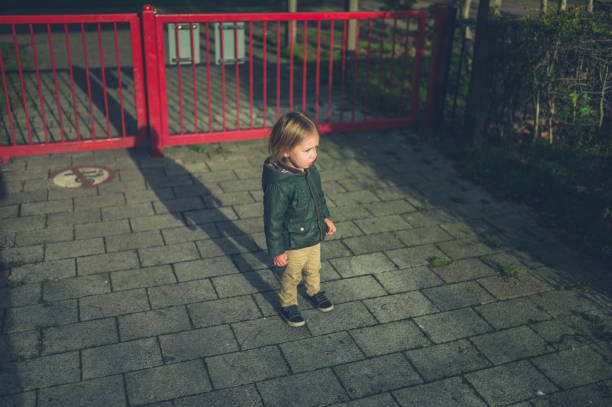 A little toddler is standing by the gate in a park
