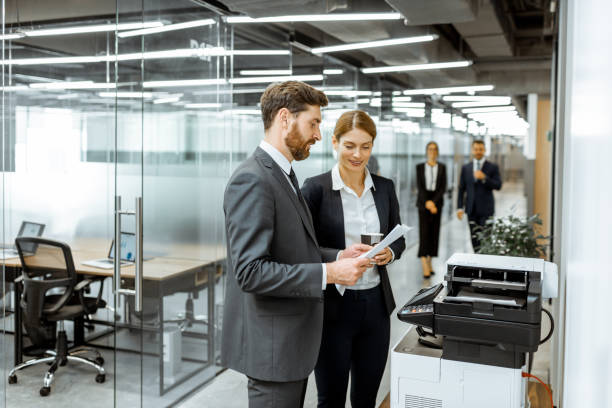 Business people near the copier in the hallway Business man and woman talking near the copier during a coffee break in the hallway of the big corporation computer printer stock pictures, royalty-free photos & images