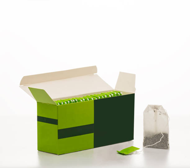 Many tea bags in wooden box and leaves on light green background, closeup