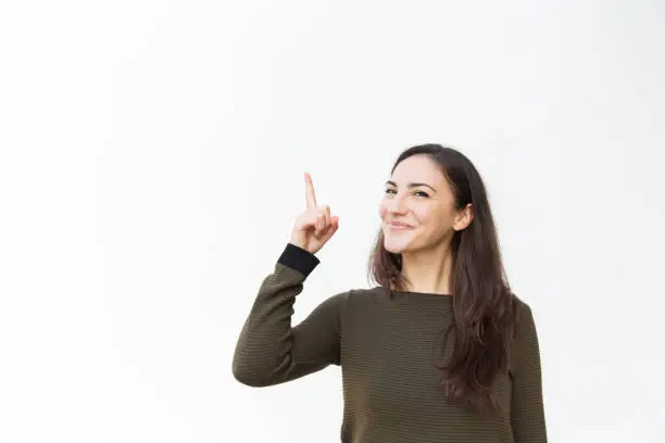Happy joyful beautiful woman pointing finger up. Young woman in casual standing isolated over white background. Having idea or advertising concept