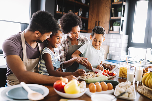 Happy african american family preparing healthy organic food together in kitchen