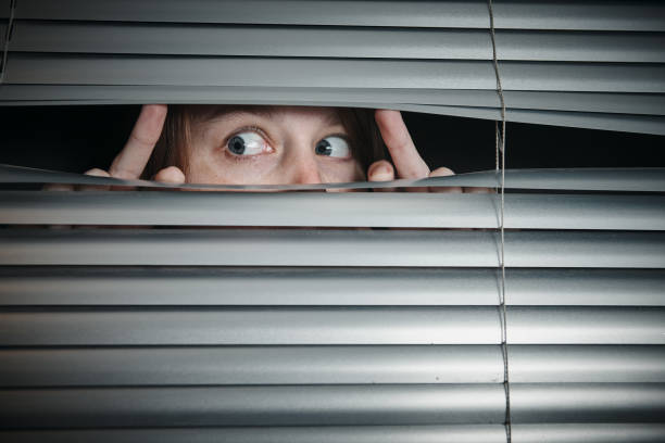 istock Startled and scared, a young woman peeps sideways through blinds 1189090906