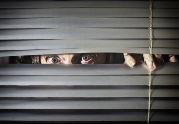 istock Nervous senior woman peers through closed blind 1189091105