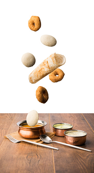 Food  Levitation - flying idli, dosa and  vada with sambhar and chutney in bowls over wooden table