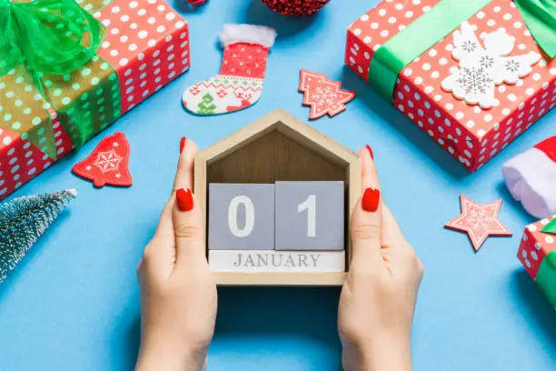 Photo of Top view of female hands holding calendar on blue background. The first of January. Holiday decorations. New Year concept