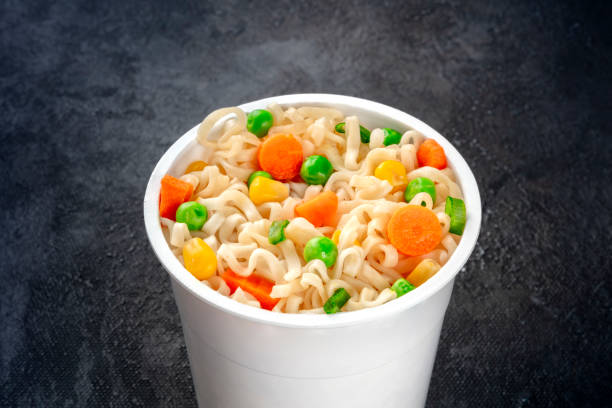 istock Ramen cup, instant soba noodles in a plastic cup with vegetables close-up on a black background 1189096731