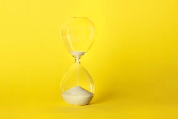 istock Time is running out concept. An hourglass with sand falling through, on a vibrant yellow background with copy space 1189096801