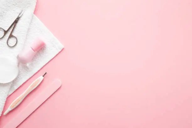 Manicure set and white towel on pastel pink table. Empty place for text or logo. Closeup. Flat lay. Top down view.