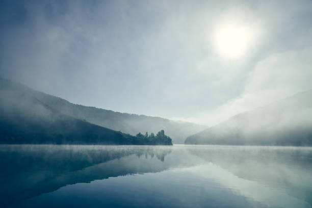 Foggy landscape. Sunrise. Nature. Lake, blue mountains and blue forest in morning. Reflection nature in water. Still blue water.