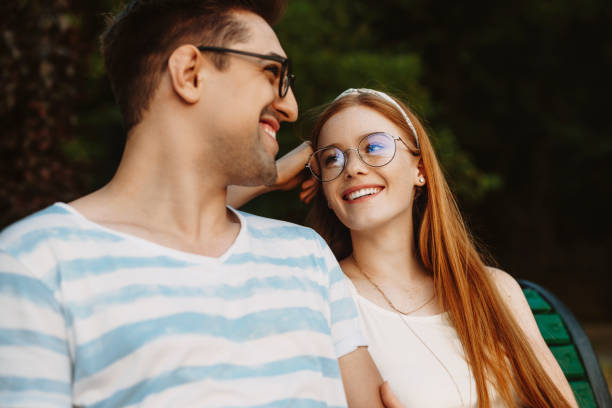 istock Close up of a charming young couple having fun laughing while sitting on a bench and looking to each other. 1189102109