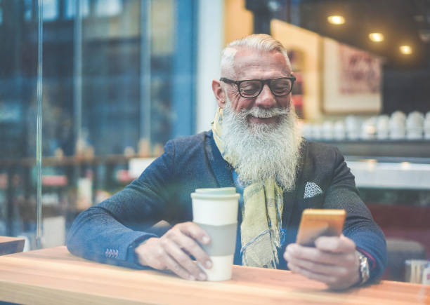 istock Senior business man using smartphone app while drinking coffee inside lounge bar - Hipster entrepreneur doing breakfast with cappuccino - Job, fashion and joyful elderly concept - Focus on face 1189102754