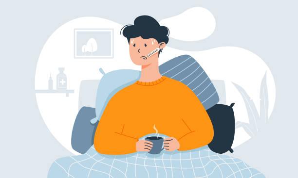 junger mann mit erkältungssymptomen wie fieber, kopfschmerzen und halsschmerzen, die die temperatur in seinem bett messen, hält eine tasse tee. - krankheit stock-grafiken, -clipart, -cartoons und -symbole