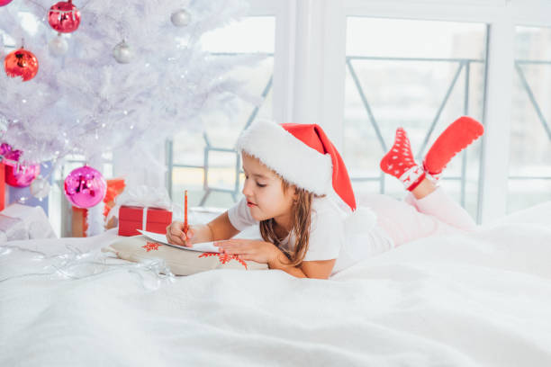 istock Inspired kid is sitting under Christmas tree, writing message to nord pole, looking pleased and hopeful. 1189113331