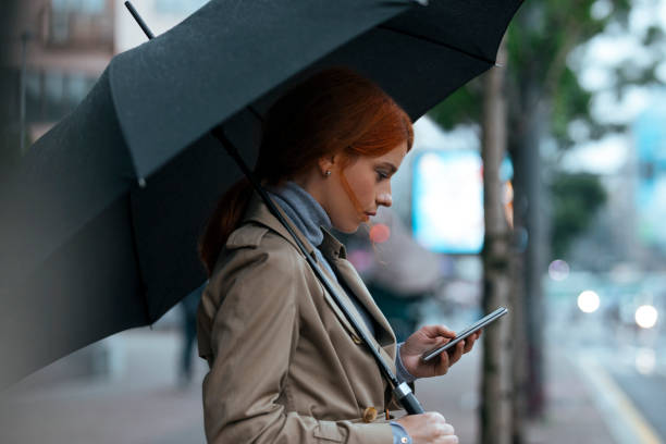 kobieta z parasolem stojącym na ulicy i wpisując telefon komórkowy - people in a row in a row business office worker zdjęcia i obrazy z banku zdjęć