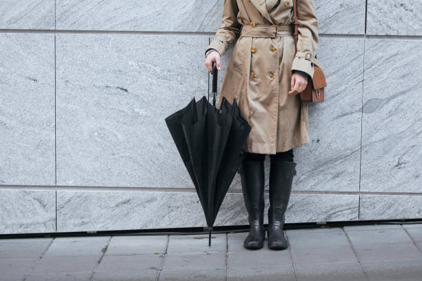 A Woman in Trench Coat Holding Umbrella Unrecognisable woman wearing trench coat and rain boots and holding umbrella while standing outdoors. rubber boot stock pictures, royalty-free photos & images