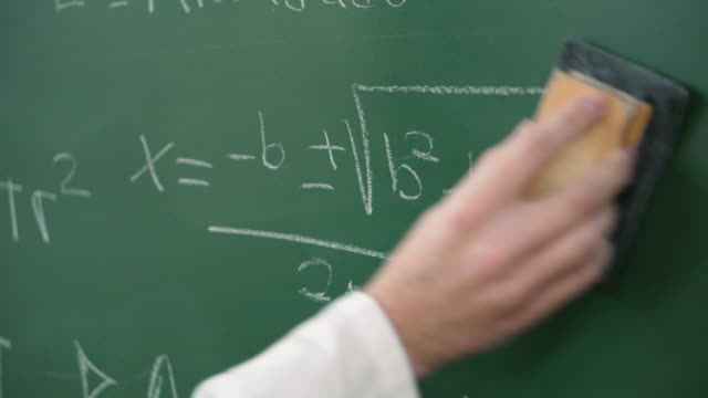 Teacher cleaning the chalkboard with maths equations.