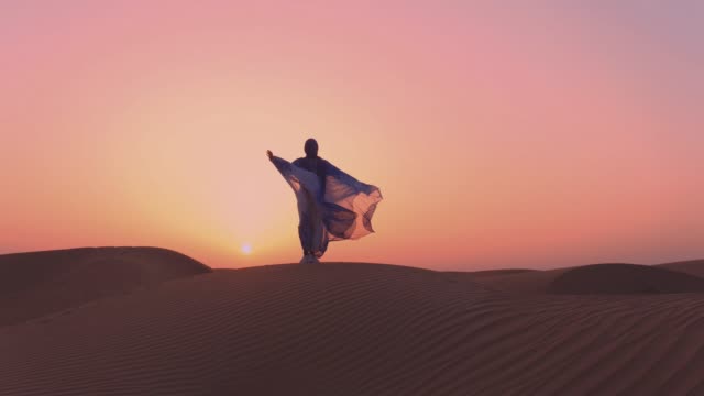 Women wearing beautiful blue and white Arab clothes rising her hands at the desert