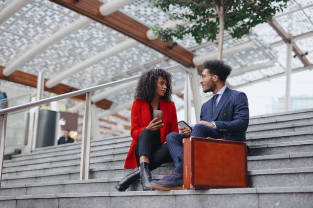 istock Young business couple using smart phone while sitting on the staircase in downtown district 1189117898