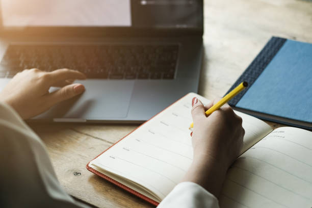 istock Woman hand with pencil writing on notebook. making notes in notebook with pencil. People writing on notebook and work on wooden table 1189119634