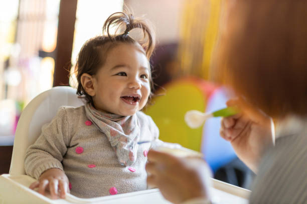 Mother feeding her baby with spoon Mother feeding her baby with spoon high chair stock pictures, royalty-free photos & images