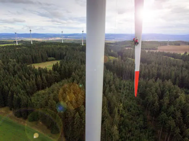 Photo of View from drone on high rise rope access technician doing inspection of blade on wind turbine