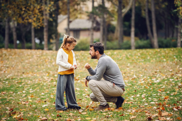 istock Devilish cute little girl with ponytail standing and looking at her father. Father crouching and reprimanding her. Autumn in park. 1189128154