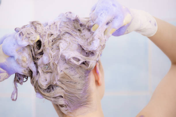 Woman applying toner shampoo on her hair Woman applying coloring shampoo on her hair. Female having purple washing product. Toning blonde color at home. shampoo stock pictures, royalty-free photos & images