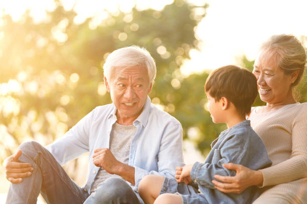 asian grandparents having fun with grandson asian grandson, grandfather and grandmother sitting chatting on grass outdoors in park at dusk china chinese ethnicity smiling grandparent stock pictures, royalty-free photos & images