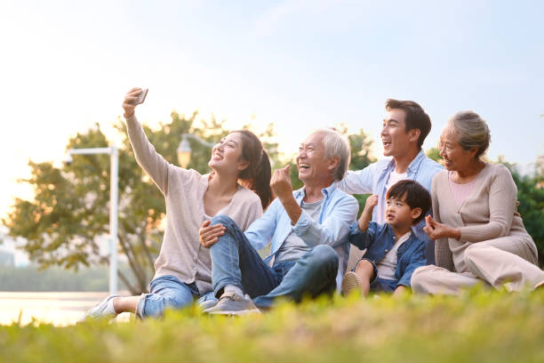 three generation asian family taking selfie outdoors three generation happy asian family sitting on grass taking a selfie using mobile phone outdoors in park china chinese ethnicity smiling grandparent stock pictures, royalty-free photos & images