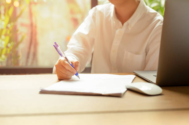 istock Hand filling document form contract with laptop an mouse on wooden table. 1189134724