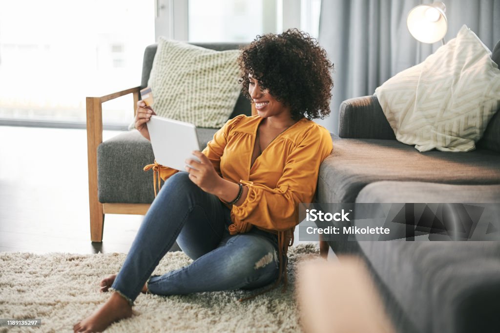 Time for some much needed retail therapy Cropped shot of an attractive young woman sitting on her living room floor and using her tablet for online shopping Women Stock Photo