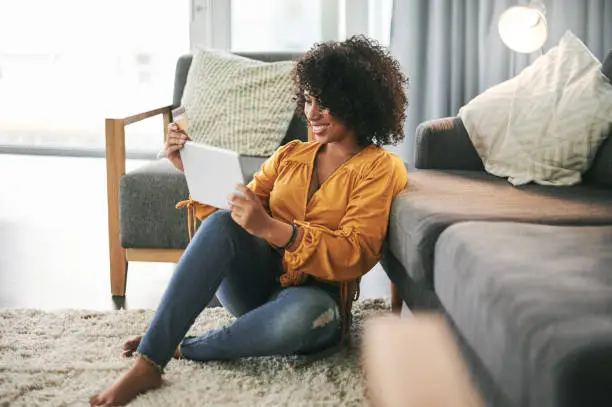 Cropped shot of an attractive young woman sitting on her living room floor and using her tablet for online shopping