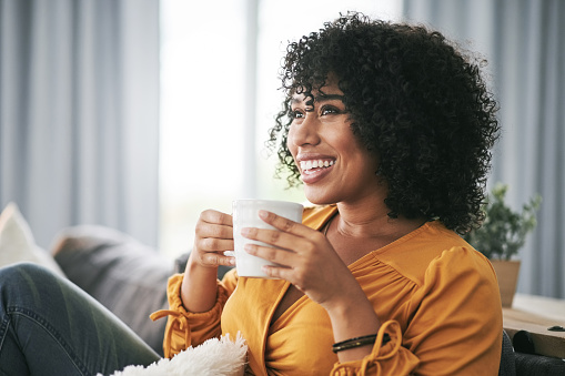 Cropped shot of an attractive young woman sitting on her sofa alone at home and holding a cup of coffee