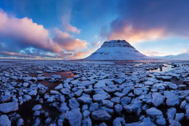 Photo of Iceland snaefellsnes peninsula and famous Kirkjufell in winter sunrise. Kirkjufell is a beautifully shaped and a symmetric mountain in Iceland. Frozen view of Kirkjufell reflection in water.