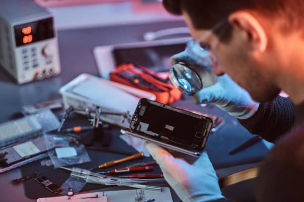 le technicien examine attentivement l'intégrité des éléments internes du smartphone dans un atelier de réparation moderne - male magnifying glass caucasian technician photos et images de collection