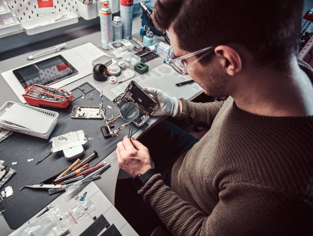 serviceman utilise un loupe et une pince à épiler pour réparer le smartphone endommagé dans l'atelier. - male magnifying glass caucasian technician photos et images de collection