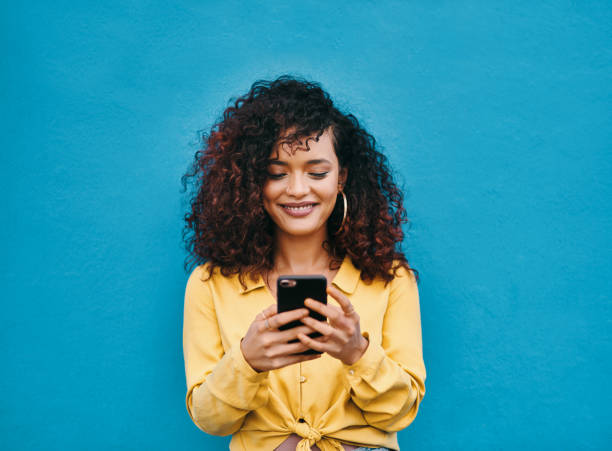 I'm loving how this conversation is going Cropped shot of an attractive young woman smiling while using a smartphone against a blue background mobile phone text messaging telephone women stock pictures, royalty-free photos & images