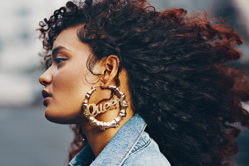 Cropped shot of an attractive young woman standing in the city while wearing an earring that has the word 