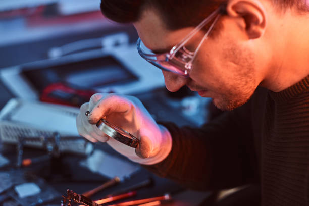 istock Electronic technician mending a broken tablet carefully examines the chip of the tablet using a magnifying glass. Illumination with red and blue lights 1189143431