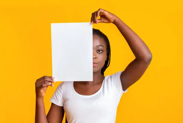 Photo of Serious girl covering half of her face with blank paper