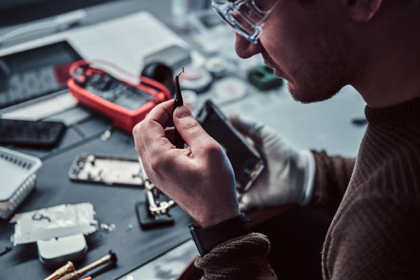 istock Electronic technician mending a broken phone, looking closely at the little bolt holding it with tweezers 1189143569