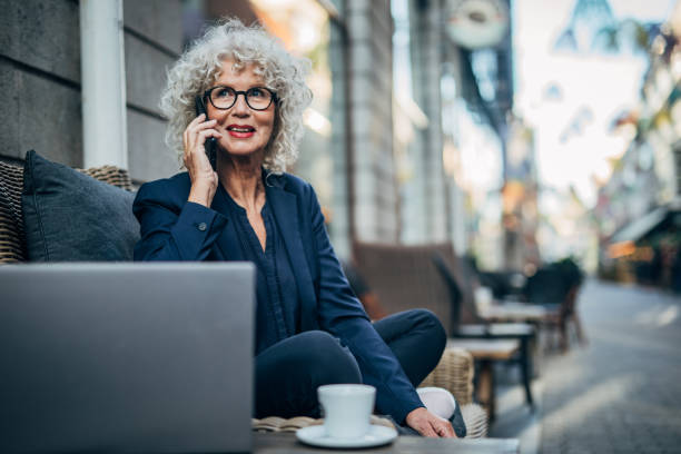 Senior lady talking on mobile outdoors in cafe One woman, modern mature lady with gray hair, talking on mobile phone in sidewalk cafe. business lifestyle stock pictures, royalty-free photos & images