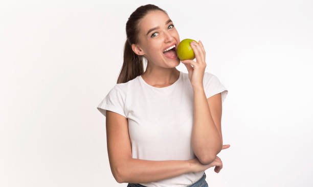istock Woman Biting Apple Looking At Camera Standing In Studio 1189146538
